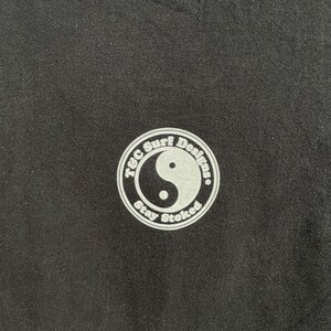 Puede incluir: Tela negra con un logotipo circular blanco. El logotipo presenta el texto "T&C Surf Designs" alrededor del borde, un s&iacute;mbolo de yin-yang en el centro y las palabras "Stay Stoked" en la parte inferior.