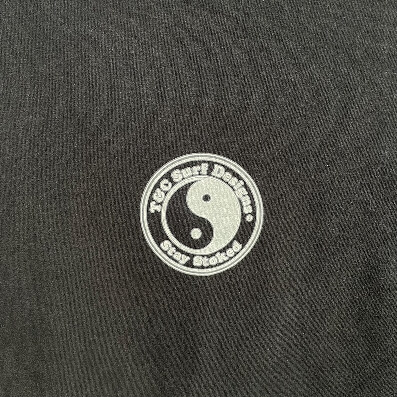 Puede incluir: Tela negra con un logotipo circular blanco. El logotipo presenta el texto "T&C Surf Designs" alrededor del borde, un s&iacute;mbolo de yin-yang en el centro y las palabras "Stay Stoked" en la parte inferior.