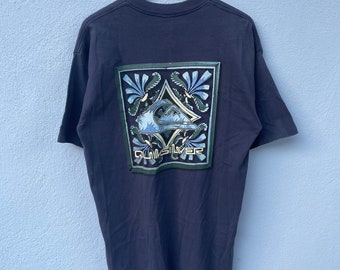 May include: A dark blue t-shirt with a graphic print of the Quiksilver logo in a green, blue, and yellow color scheme. The logo is surrounded by a decorative border.