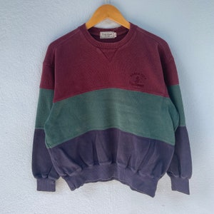 Könnte beinhalten: Ein rotbraunes, grünes und marineblaues gestreiftes Sweatshirt mit einem weißen gestickten Logo, auf dem "ATHLETIC 1905 Paul Stuart" steht.