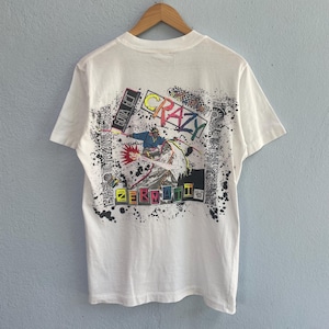 May include: White t-shirt with a colorful graphic on the back. The graphic features the word "CRAZY" in a vibrant, multi-colored font, along with an illustration of a figure in action. The shirt also has the text "ZERMATTI".