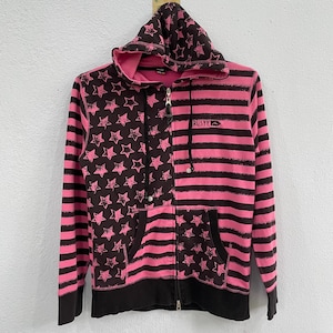 May include: A pink and black zip-up hoodie with a star pattern on the left side and horizontal stripes on the right. The hoodie has a drawstring hood, a front pocket, and the word "RUSTY" printed on the chest.