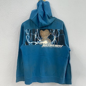 May include: A teal hoodie featuring a graphic of Astro Boy with lightning bolts and the text "ASTRO BOY" on the back. The hoodie has a hood and a kangaroo pocket. The fabric appears to be a soft, comfortable material.