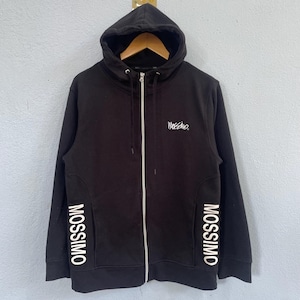 May include: A black zip-up hoodie featuring a white Mossimo logo on the left chest and the word Mossimo printed in large white capital letters vertically along both sides of the lower front. The garment includes a hood with drawstrings and a white zipper.