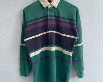 May include: A long-sleeved rugby shirt with a striped pattern in green, white, navy blue, and purple. The shirt has a button-up collar and a button placket.