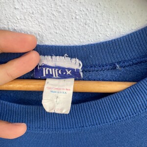 Peut inclure: Un sweat-shirt bleu avec une &eacute;tiquette de marque blanche et bleue &agrave; l'encolure int&eacute;rieure. L'&eacute;tiquette affiche le texte Tultex, avec une &eacute;tiquette blanche secondaire en dessous indiquant Care/Content On Back et Made in U.S.A. en rouge et bleu.