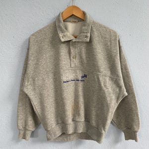 May include: A set of three ceramic mugs with a speckled, matte finish. The mugs are in shades of cream, light gray, and dark gray. Each mug has a simple, minimalist design and a rounded handle.