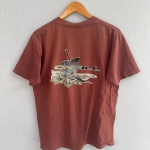 May include: A brown t-shirt featuring a graphic of a surfer riding a wave with the word "ONEILL" printed on it.