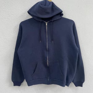 May include: A navy blue zip-up hoodie with a hood and a front pocket. The hoodie features a metal zipper and ribbed cuffs and hem. The garment is suspended against a plain white backdrop.