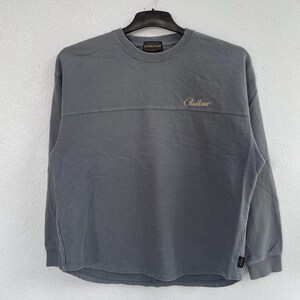 Może przedstawiać: Szara bluza z długim rękawem z okrągłym dekoltem i nazwą marki "Pendleton" wyhaftowaną kursywą. Bluza ma poziomy szew na piersi i wisi na czarnym wieszaku.