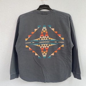 Puede incluir: Una sudadera de manga larga gris carbón con un colorido diseño geométrico en la espalda. El diseño presenta formas naranjas, amarillas, turquesas y azules dispuestas en un patrón simétrico. La sudadera está colgada de una percha negra.