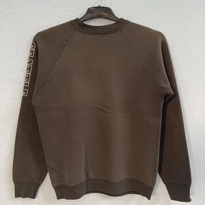 May include: A brown sweatshirt with the word "SEATTLE" printed vertically in white letters on the left sleeve. The sweatshirt has a crew neck and long sleeves. The garment is hanging on a black hanger.