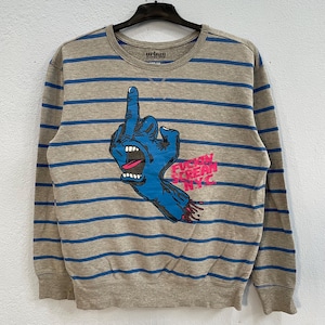 Puede incluir: Una sudadera gris con rayas horizontales azules. La parte delantera presenta un gráfico de una mano azul con el dedo medio levantado, una boca abierta y el texto "FUCKIN' SCREAM NYC" en rosa y blanco.