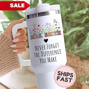 May include: White tumbler with a handle, featuring the text "MRS. SMITH" above a black heart and the phrase "NEVER FORGET THE DIFFERENCE YOU MAKE." The design includes colorful flowers and butterflies. A red "SALE" banner is visible.