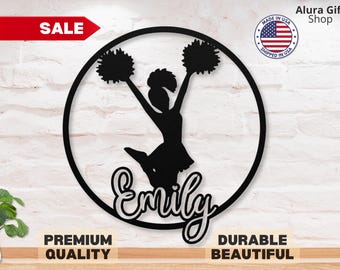 May include: Black metal wall art featuring a cheerleader silhouette with pom-poms, leaping within a circular frame. The name "Emily" is scripted below. Includes "Premium Quality" and "Durable Beautiful" text. A red "SALE" banner is in the upper left.