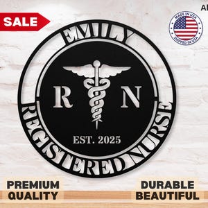 Pode incluir: Um sinal de metal preto com as palavras "Registered Nurse" que rodeiam um s&iacute;mbolo de caduceu e as letras "RN". O sinal tamb&eacute;m inclui o nome "Emily" e o ano "EST. 2025".