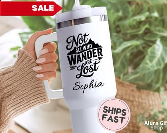 May include: White travel mug with a handle, featuring the quote "Not all who wander are lost" in black script, with a mountain and arrow graphic. The name "Sophia" is below the quote. A red "SALE" tag is in the upper left.