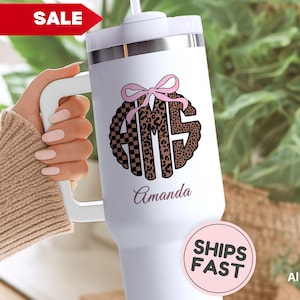May include: White tumbler with a handle, featuring a monogram design with a pink bow and leopard print accents. The name "Amanda" is printed below the monogram. A red "SALE" banner is visible.
