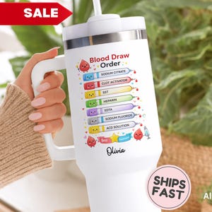 May include: White insulated tumbler with a handle, featuring a "Blood Draw Order" chart with colorful illustrations and text. The tumbler includes the name "Olivia" and a "Ships Fast" sticker.
