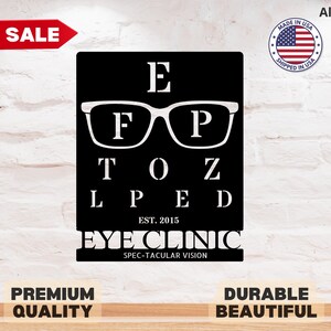 May include: Black eye chart sign with white text and glasses graphic. The sign reads "E F P TOZ L P E D" and "EYE CLINIC SPEC-TACULAR VISION". Includes "EST. 2015" and a "Made in USA" sticker.
