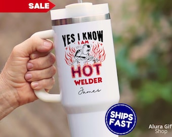 May include: White travel mug with a handle, featuring the text "YES I KNOW I AM HOT WELDER" with a graphic of a welder and flames. The name "James" is below the text. A red "SALE" banner is in the top left.