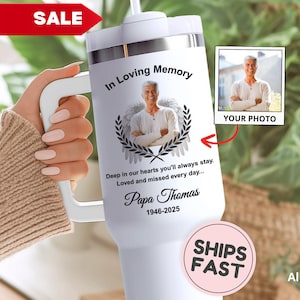 May include: White travel mug with a photo and the text "In Loving Memory." The mug features a picture of a person with angel wings, a laurel wreath, and the text "Papa Thomas 1946-2025." A red "SALE" banner is in the upper left.