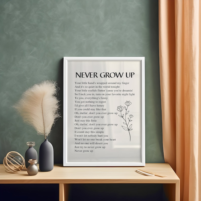 May include: A white framed print with a black and white design. The print features a poem titled "Never Grow Up" with a simple floral illustration. The poem encourages staying young at heart.
