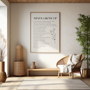 May include: A black and white printable wall art print with the lyrics to the song "Never Grow Up". The lyrics are printed in a simple font and are centered on the page. A simple floral design is in the bottom right corner of the print.