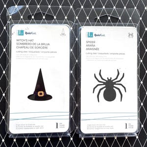 May include: Two QuickKutz cutting die packages in clear plastic. The left package features a black witch's hat with a purple band and gold buckle. The right package features a black spider silhouette. Both include text labels and die counts.