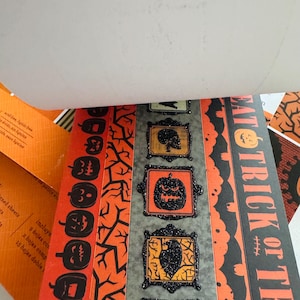 K&ouml;nnte beinhalten: Ein dekorativer Papierblock mit Halloween-Motiven in Orange und Schwarz. Die Seiten zeigen Muster von K&uuml;rbissen, kahlen &Auml;sten und gerahmten Symbolen von Totenk&ouml;pfen und Raben. Der Text EAT TRICK OR TREAT ist vertikal aufgedruckt.