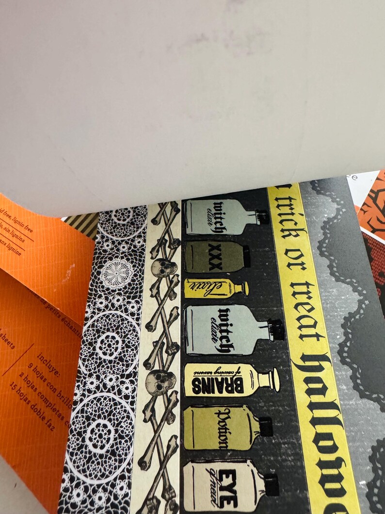 K&ouml;nnte beinhalten: Ein dekoratives Papierblatt mit einem vertikalen Muster aus Totenk&ouml;pfen und Knochen, einer Reihe beschrifteter Zaubertrankflaschen und einem gelben Streifen mit dem Text trick or treat halloween. Das Design enth&auml;lt ein schwarz-wei&szlig;es Spitzenmuster.