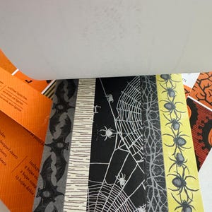 K&ouml;nnte beinhalten: Ein Papierblock mit verschiedenen Halloween-Mustern, darunter schwarze Flederm&auml;use auf grauem Grund, eine wei&szlig;e Birkenrindenstruktur, wei&szlig;e Spinnennetze auf schwarzem Grund, graue Baumzweige und schwarze Spinnen auf gelbem Grund.