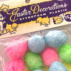 May include: A package of colorful Easter decorations. The package contains styrofoam eggs in pink, blue, and green. The packaging reads "Easter Decorations" with illustrations of chicks and bunnies.