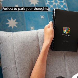 May include: A black spiral-bound notebook with a colorful Rubik's Cube graphic and the text "UNSORTED DATA." The notebook is held by a person. The text "Perfect to park your thoughts" is at the top.