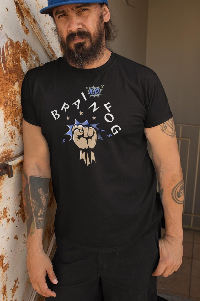 May include: Black crew neck t-shirt with the words "BRAIN FOG" in a stylized font, featuring a fist graphic. The design includes blue and white accents. The shirt is worn by a person wearing a blue cap.
