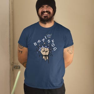 May include: Navy blue t-shirt with the text "BRAIN FOG" in a comic book style. The design includes a clenched fist and stars. The person in the image is wearing a black beanie and black pants.