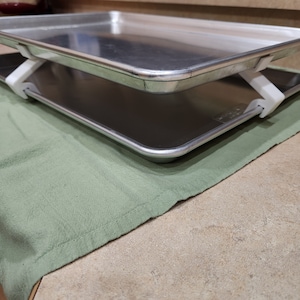 Könnte beinhalten: Zwei silberne Backbleche mit weißen Clips, die sie zusammenhalten. Die Backbleche liegen auf einem grünen Tuch.
