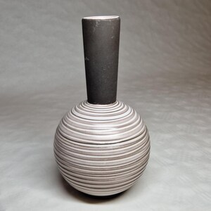 Könnte beinhalten: Eine Keramikvase mit kugelförmigem Boden und zylindrischem Hals. Der Boden ist weiß mit horizontalen grauen Streifen. Der Hals ist dunkelgrau. Die Vase ist ein dekorativer Gegenstand.