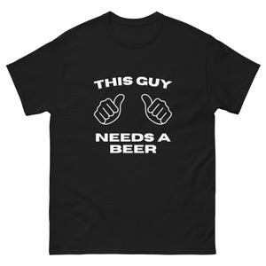 Könnte beinhalten: Schwarzes T-Shirt mit dem weißen Text "THIS GUY NEEDS A BEER" und zwei Daumen hoch. Ein lässiges Kleidungsstück, ideal für Freizeitaktivitäten. Das Design ist schlicht und auffällig.