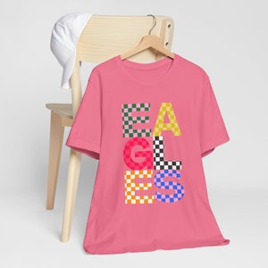 Pode incluir: Camiseta rosa com um gráfico "EAGLES" xadrez em várias cores.