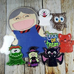 May include: A collection of Halloween-themed felt appliques, including a smiling ghost, owl, cat, bat, witch, and monster. The central piece is a large, smiling face with glasses and a blue outfit. A sign reads "Trick or Treat".