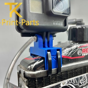 Könnte beinhalten: Ein blauer 3D-gedruckter GoPro-Kamerahalter mit dem Text "TK-Print-Parts" und "GoPro" darauf gedruckt. Der Halter ist an einem schwarzen und roten Motor mit dem Text "ROTAX RACING" befestigt.