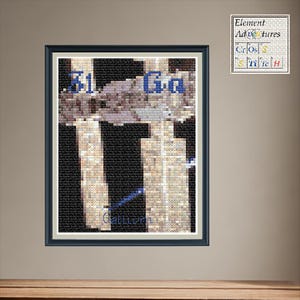 Op de afbeelding: Een ingelijst kruissteekkunstwerk met het element Gallium, met het symbool 'Ga' in blauw. Het kunstwerk heeft een zwarte achtergrond en een witte rand, met de tekst 'Element Adventures Cross Stitch' rechtsboven.