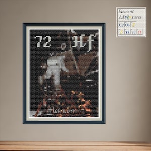May include: Framed cross-stitch art featuring the element Hafnium. The artwork displays the number 72 and the element symbol Hf. The background is dark with a pixelated appearance. The artwork is displayed on a wall with a small Element Adventures Cross Stitch sign.