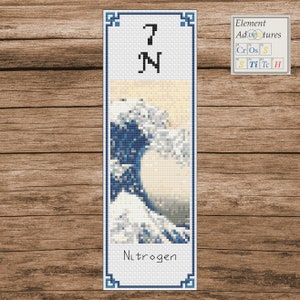 Puede incluir: Un marcapáginas con un diseño de punto de cruz de la Gran Ola de Kanagawa de Hokusai. El marcapáginas es blanco con puntadas azules y blancas. El marcapáginas tiene un borde de cuadrados negros. El marcapáginas también tiene el número 7 y la letra N en negro. El texto "Nitrogen" está debajo de la imagen. El texto "Element Adventures" está en la esquina superior derecha del marcapáginas.