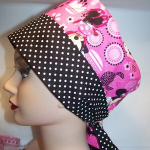 May include: A pink and black patterned surgical scrub hat with white polka dots. The hat has a tie that can be tied at the back of the neck.