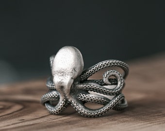 May include: A silver octopus ring with detailed tentacles. The ring is on a wooden surface.