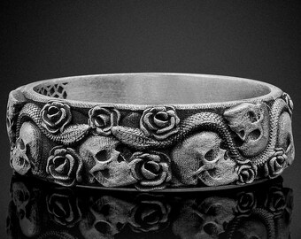 Könnte beinhalten: Ein silberner Ring mit einem detaillierten Design aus verschlungenen Schlangen, Schädeln und Rosen. Der Ring ist ein Statement-Piece mit einer gotischen Ästhetik.