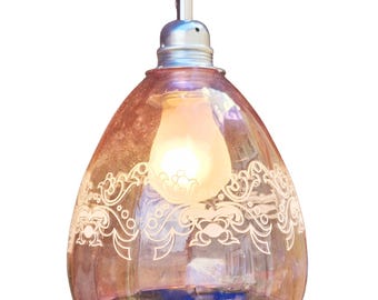 Könnte beinhalten: Dekorative Pendelleuchte mit einem tropfenförmigen, rosafarbenen Glasschirm. Der Schirm hat ein weißes, verziertes Blumendesign und beherbergt eine leuchtende Glühbirne. Das Licht hängt an einem weißen Kabel und einer silberfarbenen Halterung.