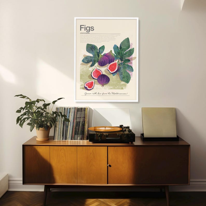 Op de afbeelding: Een ingelijste kunstdruk met een vijgenillustratie. Het kunstwerk toont hele en gesneden vijgen met groene bladeren tegen een beige achtergrond. Het woord "Figs" staat bovenaan, met tekst eronder. De print wordt boven een houten kast getoond.